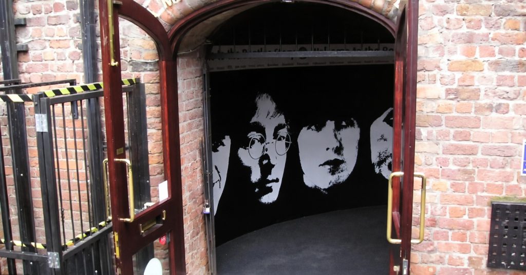 “Entrance to The Beatles Story exhibition featuring black-and-white portraits of John Lennon and Paul McCartney on a curved wall inside a brick-lined doorway.”
